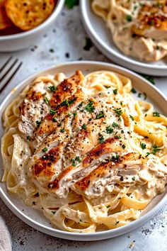 two white plates filled with chicken alfredo and pasta on top of a marble countertop