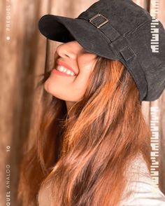 a woman with long hair wearing a black hat and smiling at the camera while standing in front of a wooden wall