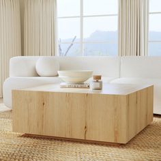 a white couch sitting next to a wooden table in a living room with large windows