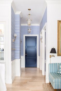 a blue and white striped wall in a hallway with a couch, lamp and painting on the wall