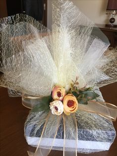 a gift wrapped in white and gold ribbon with flowers on the top, sitting on a table