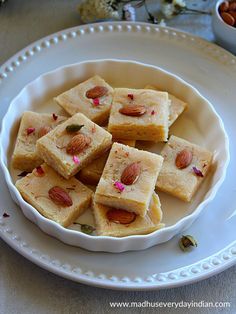 a white plate topped with pieces of cake on top of a table next to nuts