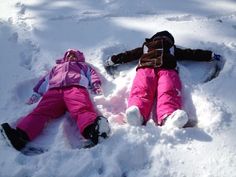 two children are laying in the snow on their stomachs and feet, one is wearing pink