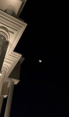 the moon is visible in the night sky above a building with columns and pillars on it