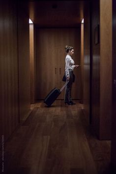 a woman standing in an empty hallway with her luggage and looking at the door to another room