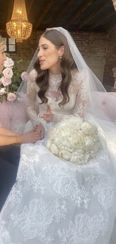 two women in wedding gowns sitting on a couch talking to each other while one woman holds her hand out