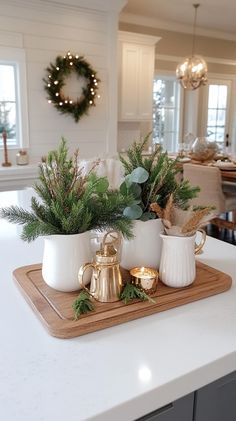 a tray with two mugs and some greenery on it in the middle of a kitchen