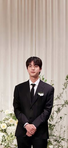 a man in a suit and tie standing next to a flower arrangement with white flowers