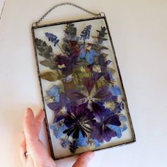 a hand is holding a glass frame with pressed flowers in it and hanging on the wall