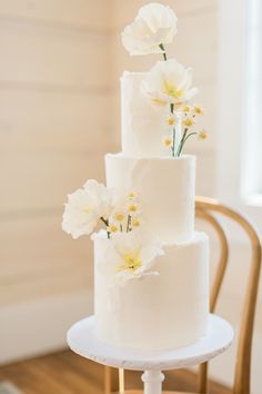 a three tiered white wedding cake with flowers on the top and bottom, sitting on a table