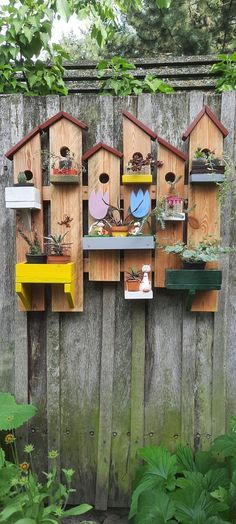 several birdhouses are mounted to the side of a wooden fence with plants growing in them