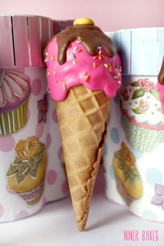 two ice cream cones with pink frosting and sprinkles are in front of cupcakes