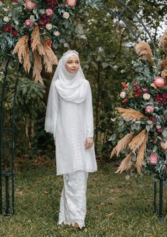 a woman wearing a white hijab standing in front of a floral arch