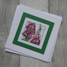 two cross stitch cards with flowers on them, one is green and the other is pink