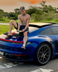 a man sitting on the hood of a blue sports car with his feet up in the air