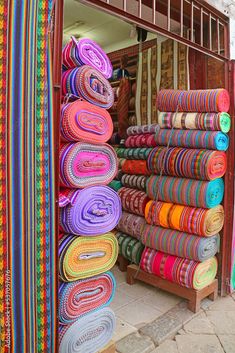 colorful rugs are stacked up in front of a store window on the side of a street