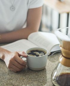 a person sitting at a table with an open book and a cup of coffee in front of them