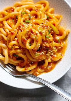 a white bowl filled with pasta and sauce on top of a table next to a fork