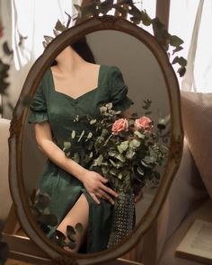 a woman in a green dress holding a bouquet of flowers looking at herself in the mirror