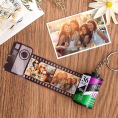 a camera keychain sitting on top of a wooden table next to pictures and flowers