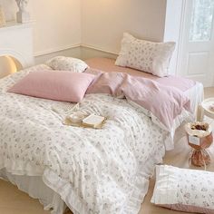 a bed with pink and white comforters on top of it next to a night stand