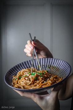 someone holding a plate of noodles with chopsticks