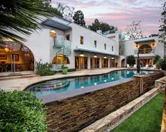 a house with a swimming pool in the middle of it and landscaping around it at dusk