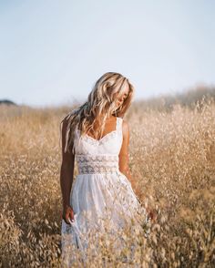 a woman in a white dress walking through tall grass