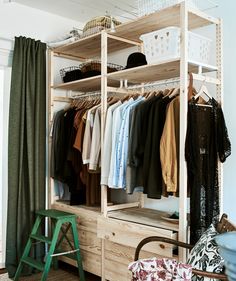 an open closet with clothes hanging on shelves and a green stool in front of it