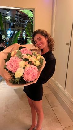 a woman holding a bouquet of pink and white flowers in her hands while smiling at the camera