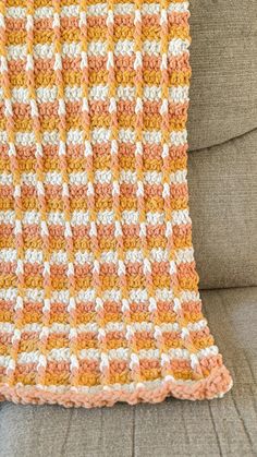 an orange and white crocheted blanket sitting on top of a couch next to a pillow