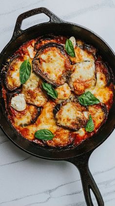 an iron skillet filled with cheese and spinach covered in sauce on top of a marble counter