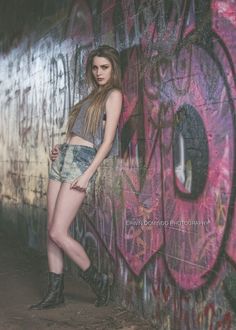 a woman standing in front of a wall covered in graffitti and wearing short shorts