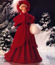 a crocheted doll wearing a red dress and hat in the snow with white pom - poms