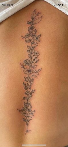 a woman's lower back tattoo with flowers and leaves on the side, in black ink