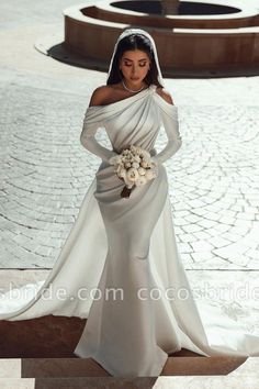 a woman in a white wedding dress standing on steps with her hands on her hips