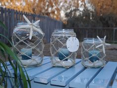 three glass jars filled with sand and seashells on top of a blue table