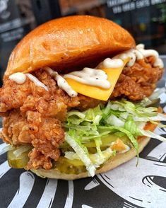 a fried chicken sandwich with lettuce and cheese on a bun sitting on top of a table