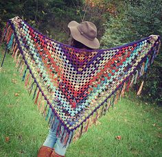 a woman wearing a hat and holding a crocheted shawl in the grass