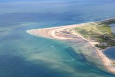 an island in the middle of water with sand on it's shore and blue sky above