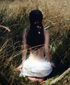 a woman with long black hair wearing a white dress sitting in the middle of tall grass