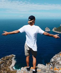 a man standing on the edge of a cliff with his arms outstretched in front of him