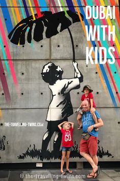 a man and two children standing in front of a wall with a painting on it