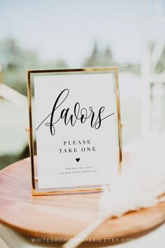 a sign that says favors please take one sitting on top of a wooden table with feathers