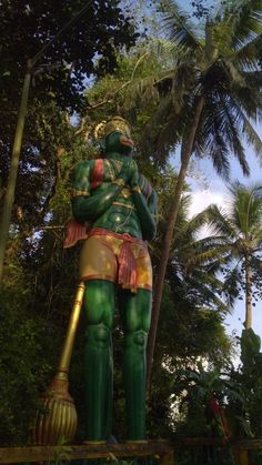 there is a statue that looks like a man holding a broom in front of palm trees