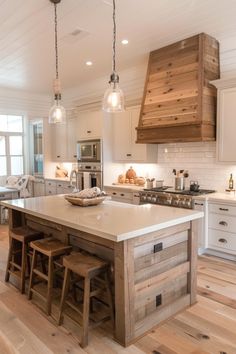 a large kitchen island with stools in the center and lights hanging from the ceiling