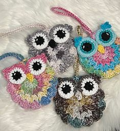 four crocheted owl purses are on a white furnishing area, one has an eyeball in the center