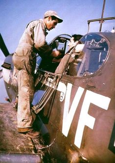 a man standing in the cockpit of an old fighter plane while another man looks on