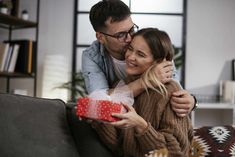 a man and woman hugging each other while holding a red gift box in front of them