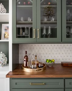 a kitchen with green cabinets and gold trim on the countertop, along with wine glasses